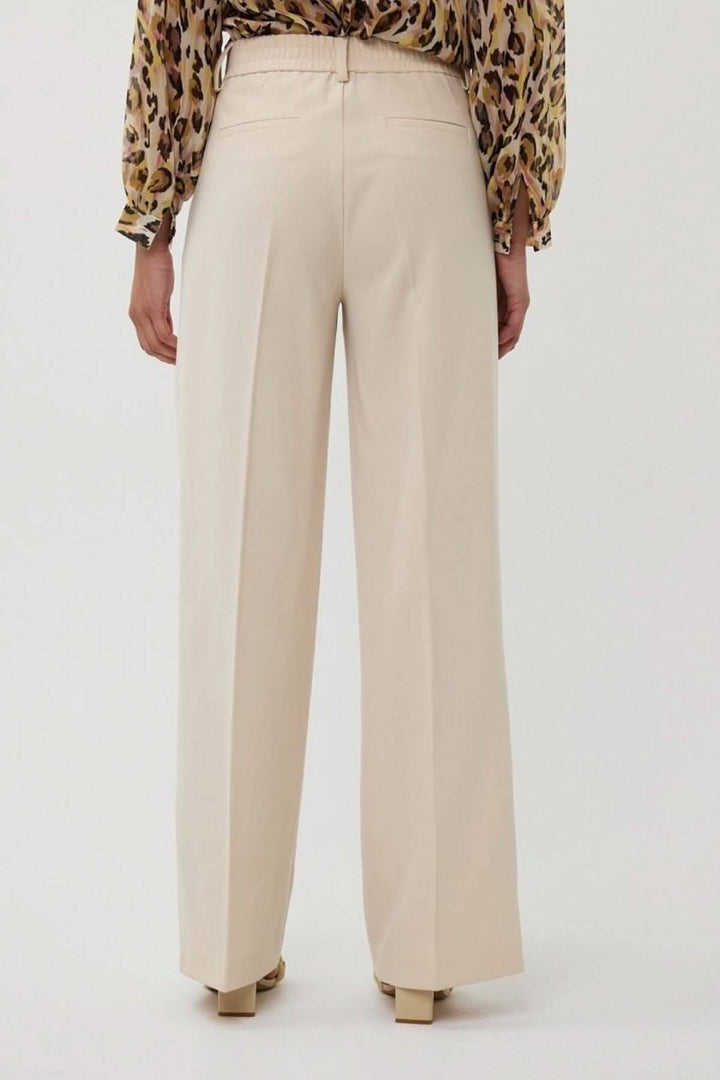 Pantalon à jambe large beige avec taille haute et plis, porté vue arrière, idéal pour un look professionnel.