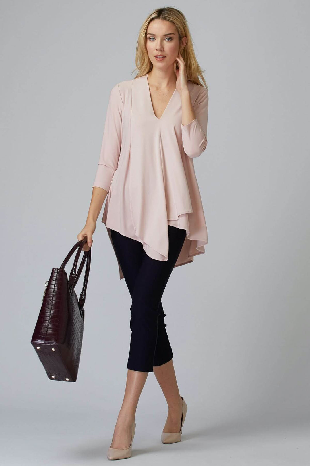 Femme portant un haut en rose pâle et un pantalon ajusté avec un sac à main, mode contemporaine.