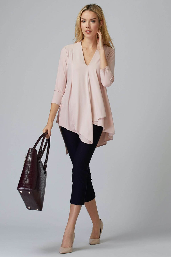 Femme portant un haut en rose pâle et un pantalon ajusté avec un sac à main, mode contemporaine.