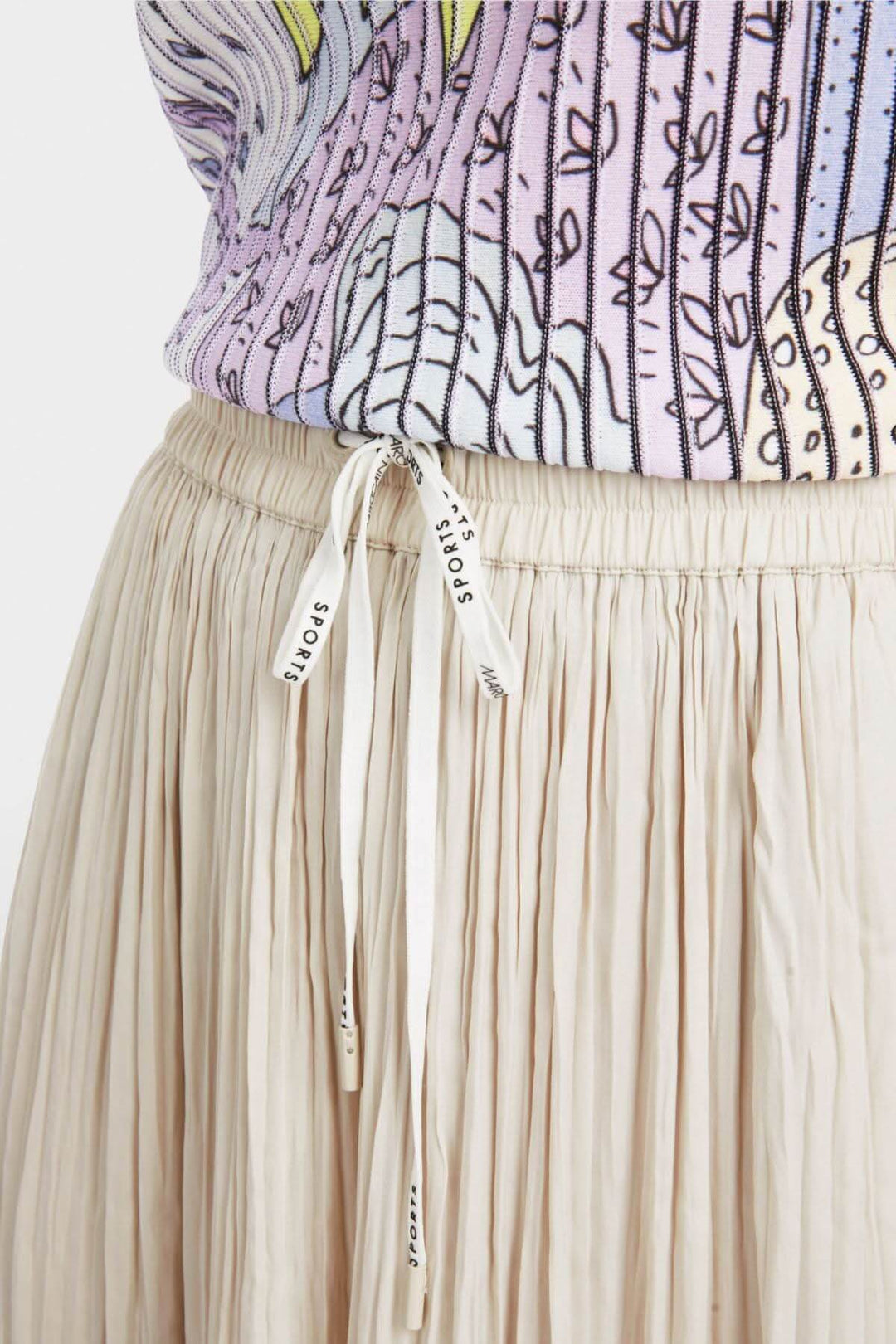 Détail d'un pantalon plissé beige avec cordon de serrage, porté avec un haut coloré, style décontracté.