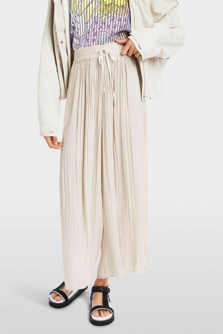 Pantalon large Wolin beige en matière fluide avec plis marqués et taille élastiquée, offrant confort et élégance.