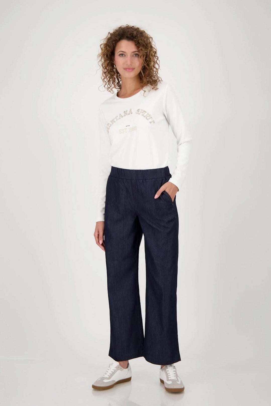 Femme portant un pantalon large en denim avec taille élastiquée et un haut blanc, parfait pour un style décontracté.