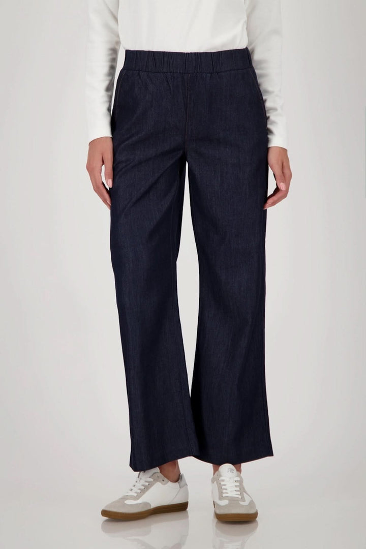 Pantalon large en denim avec taille élastiquée, coupe fluide et poches latérales, porté avec des chaussures blanches.