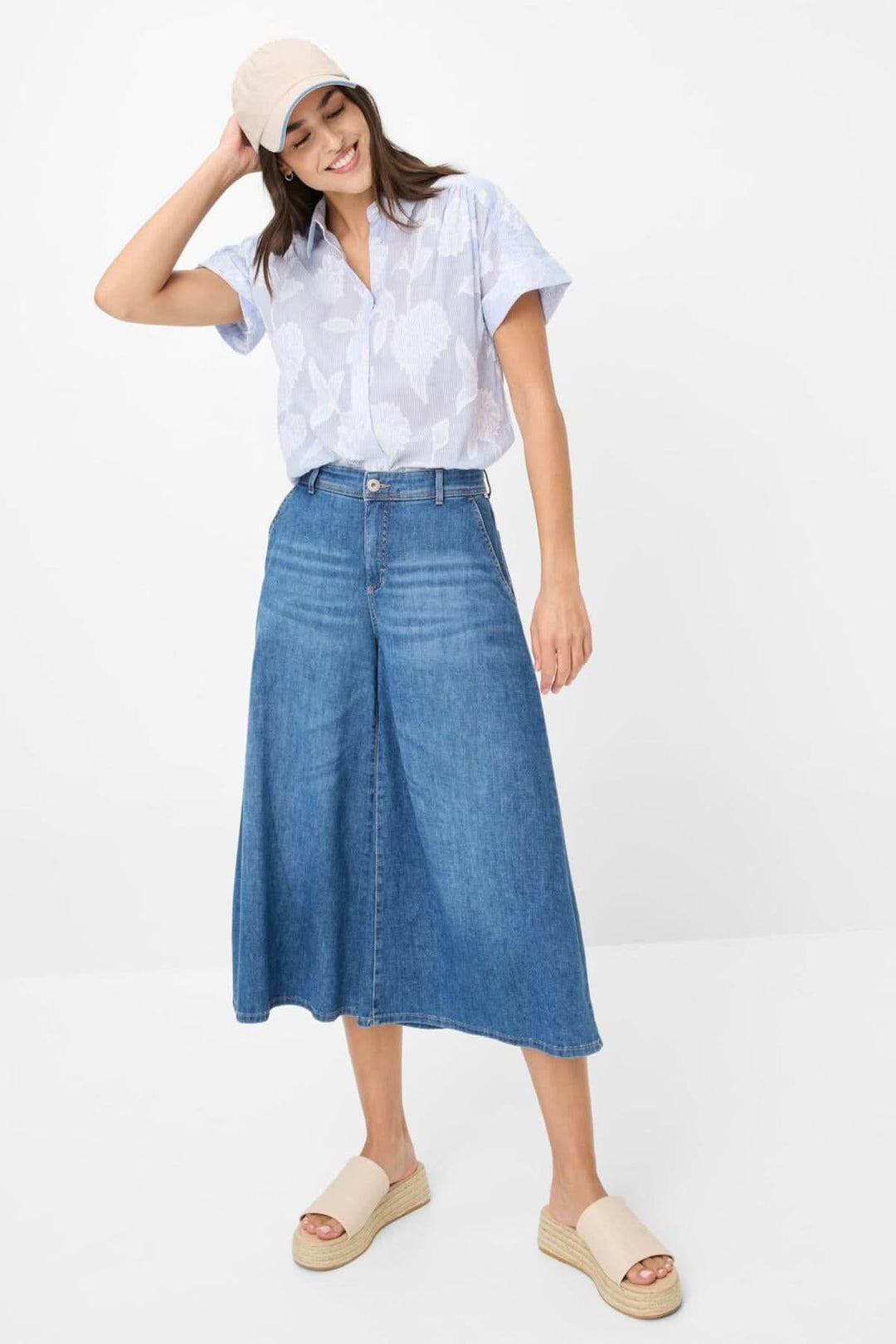 Femme portant une jupe en denim avec un haut à motifs, des sandales à plateforme et un chapeau, au style décontracté.