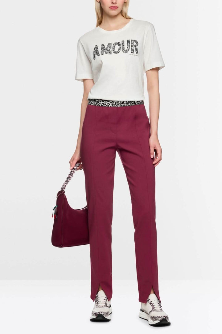 Femme portant le pantalon pull-on SIENA coupe slim avec fente frontale, associé à un haut blanc imprimé et accessoires assortis.