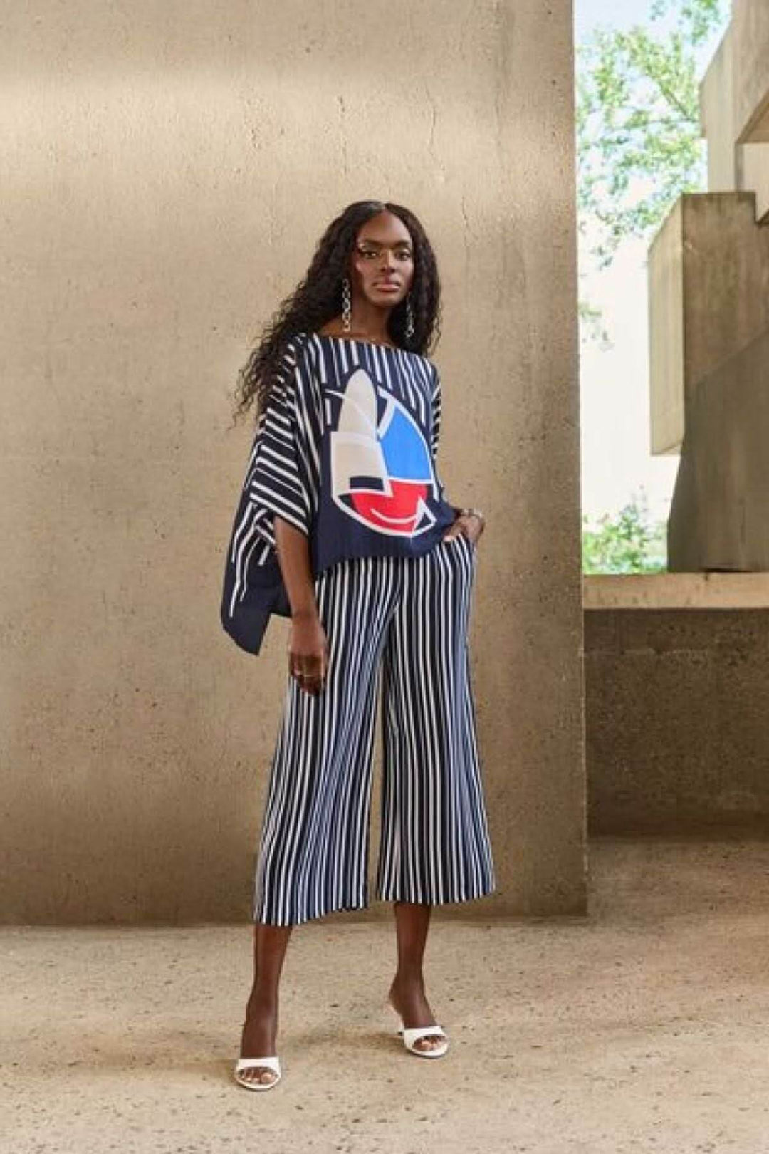 Modèle féminine en pantalon rayé évasé et top graphique, pose élégante dans un cadre moderne.