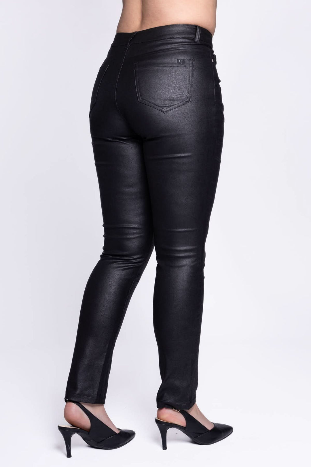Pantalon simili cuir extensible noir, coupe ajustée, avec 5 poches, porté avec des escarpins.