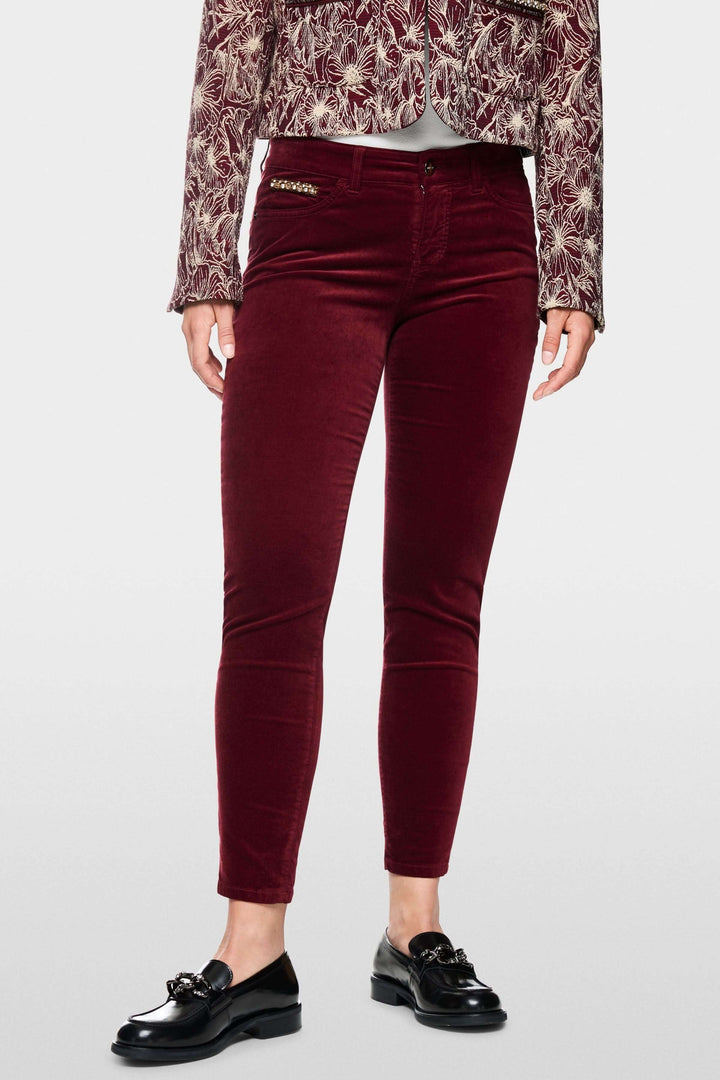 Pantalon taille basse en velours bordeaux, coupe ajustée, porté avec une veste élégante.