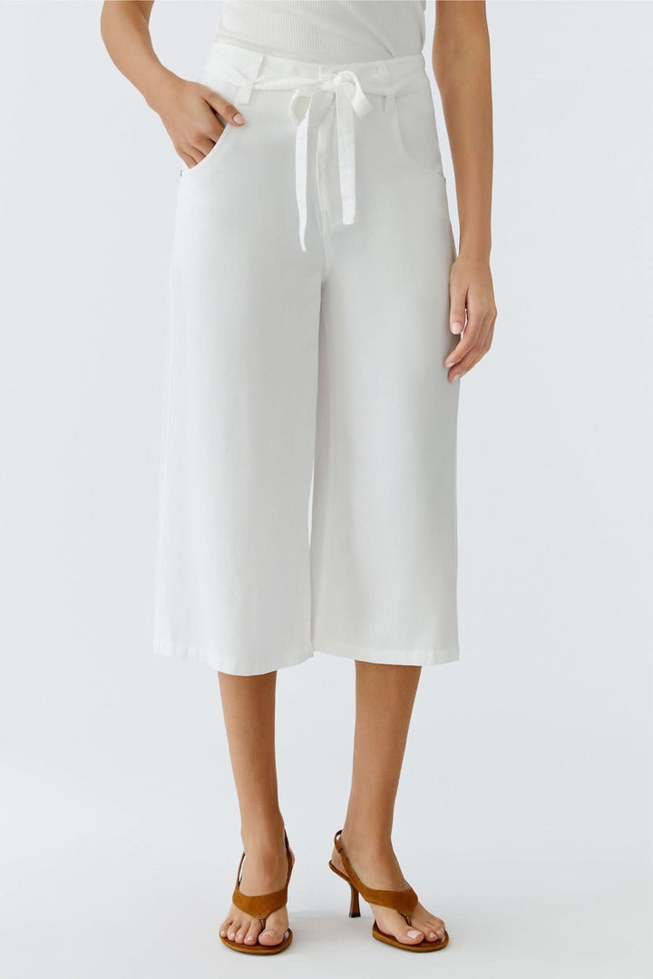 Pantalon trois quarts à taille nouée blanc avec coupe large et fluide, parfait pour la saison estivale, porté avec des sandales.