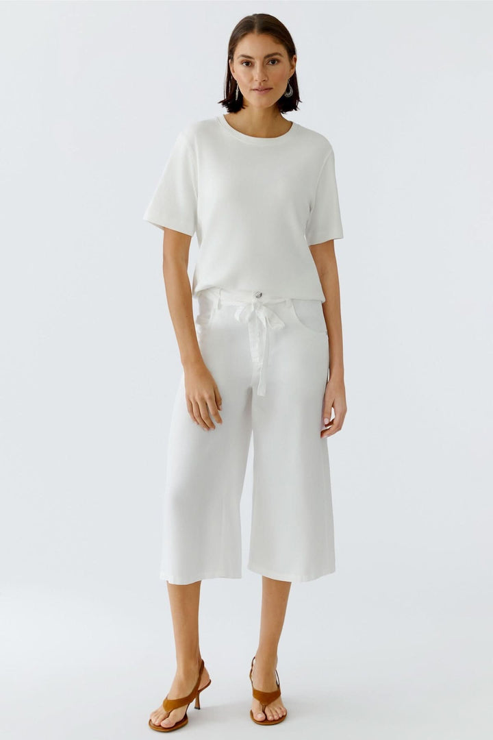 Pantalon trois quarts à taille nouée blanc porté par un mannequin, silhouette fluide et moderne, idéal pour la saison estivale.
