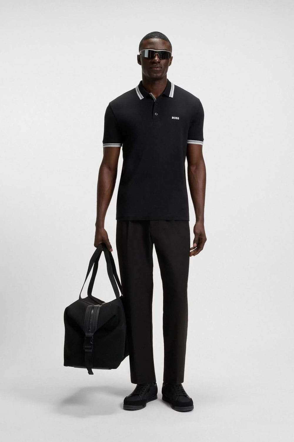 Homme portant un polo noir minimaliste avec des finitions contrastantes, stylé pour un look décontracté ou élégant.