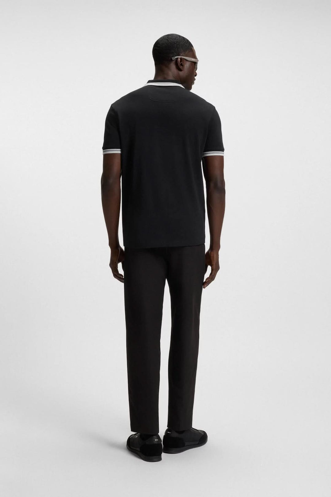 Homme portant un polo minimaliste noir avec col contrastant et pantalon noir, vue de dos.
