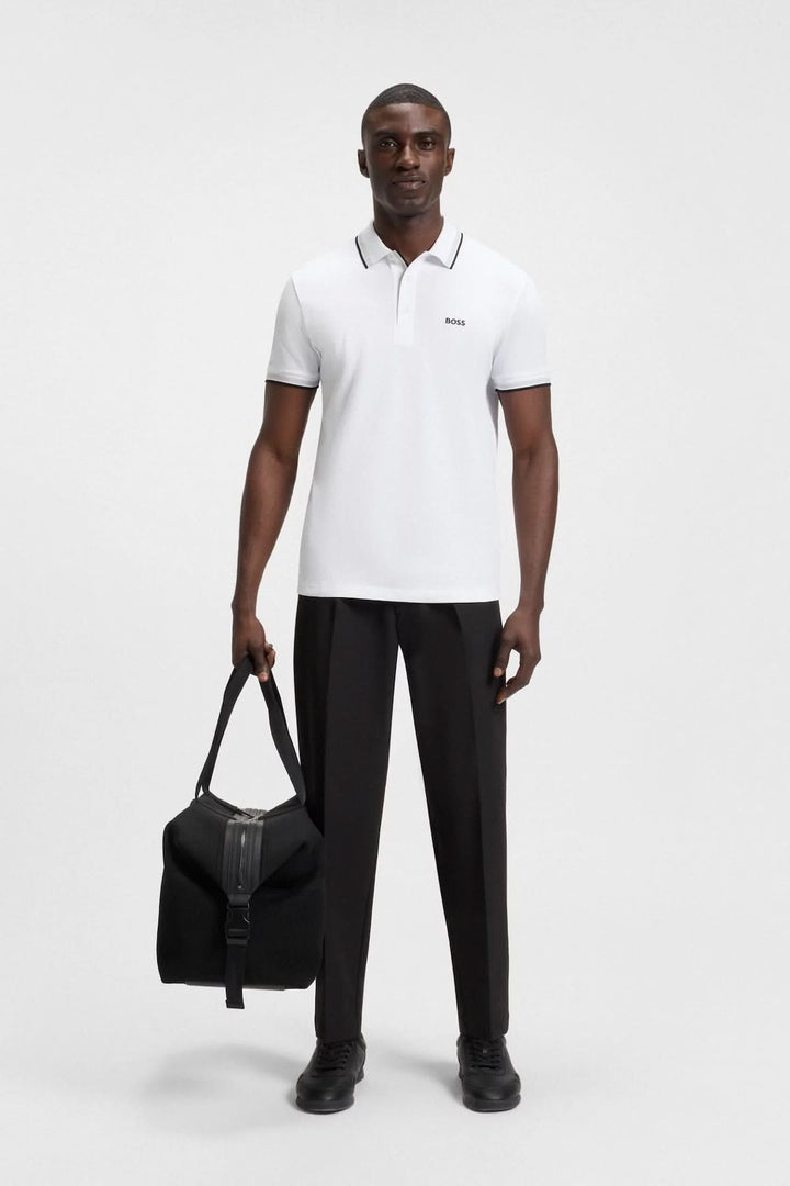 Homme portant un polo minimaliste blanc avec finitions contrastantes, associé à un pantalon noir et un sac.