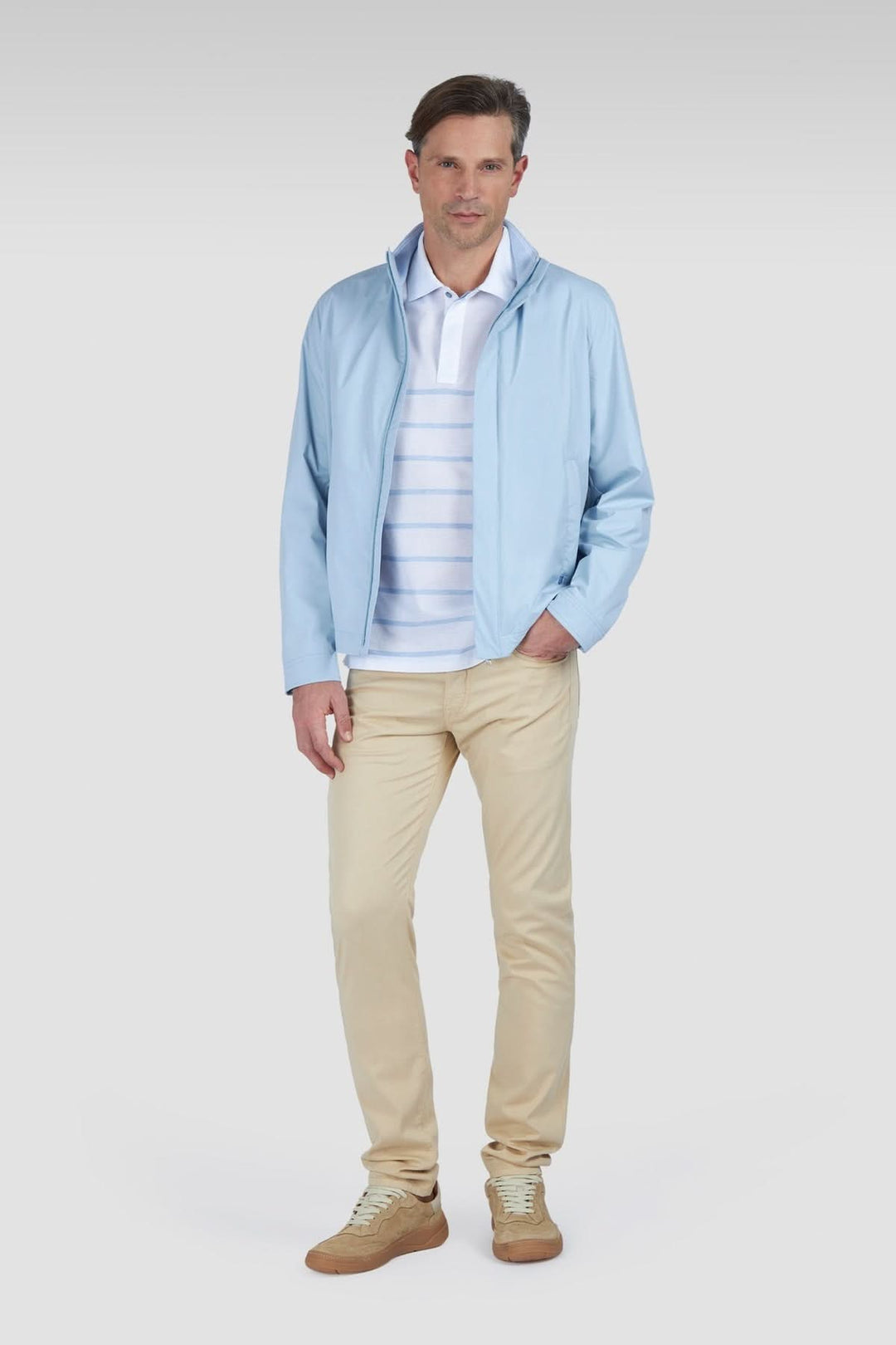 Homme portant un polo en coton piqué à rayures dégradées, veste légère, et chino beige.