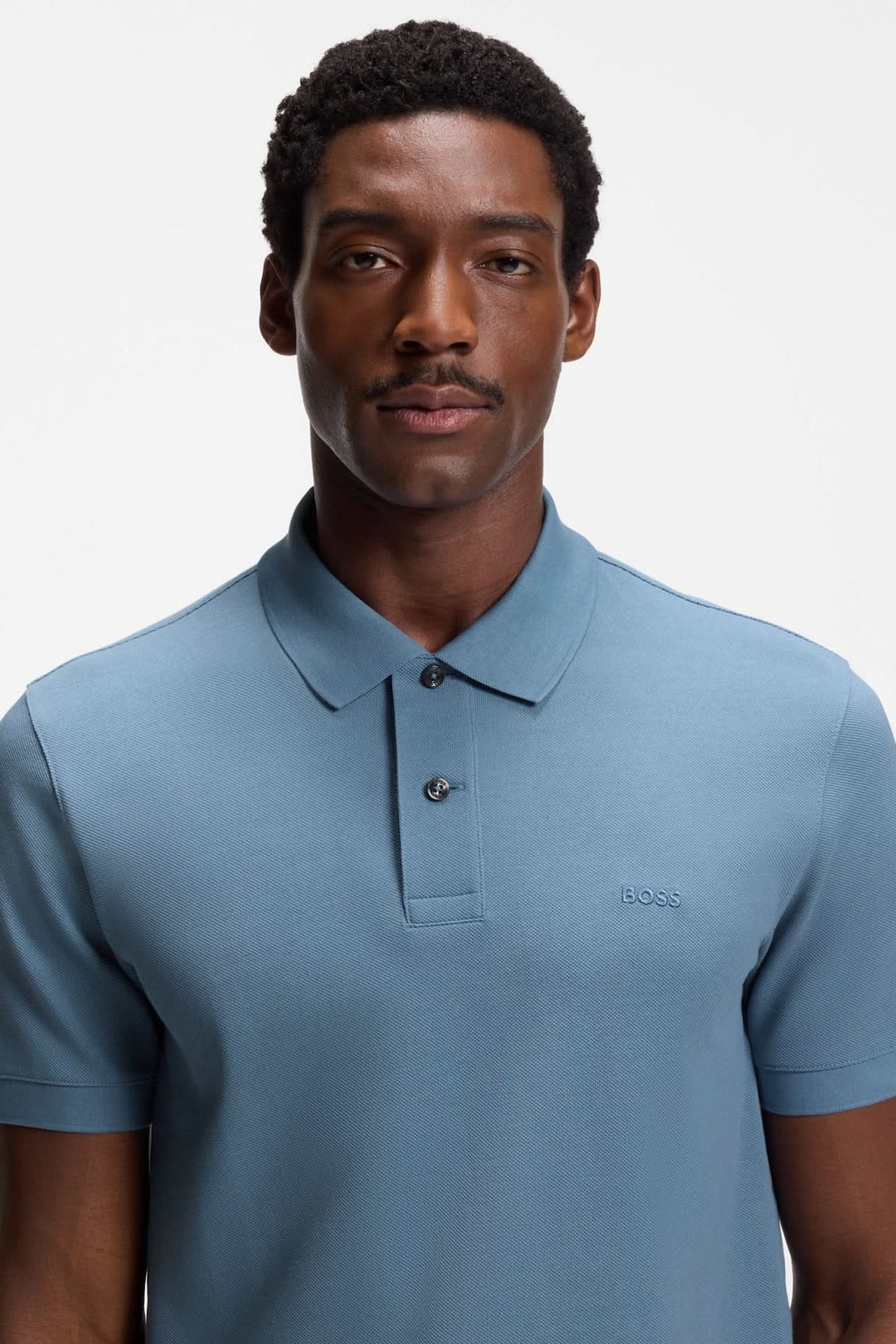 Homme portant un polo en coton piqué à logo brodé, bleu, à manches courtes, idéal pour un look décontracté ou soigné.