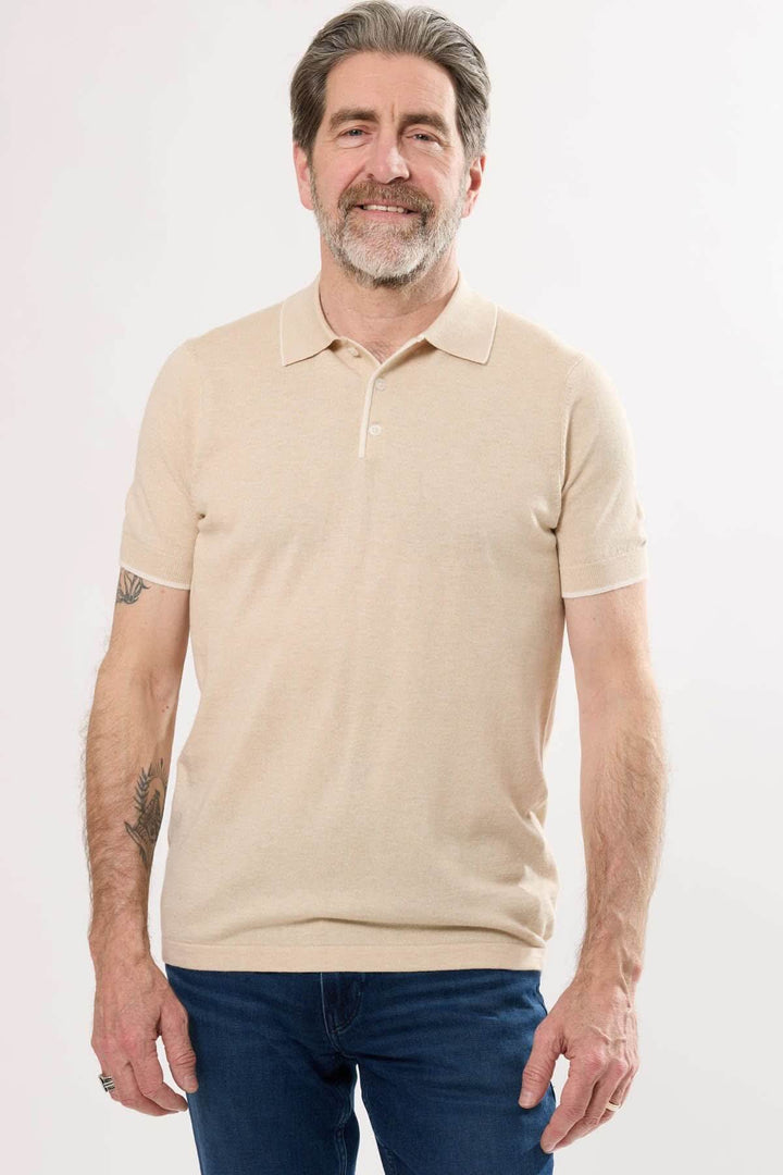 Homme souriant portant un polo en tricot fin beige avec manches courtes et col classique.