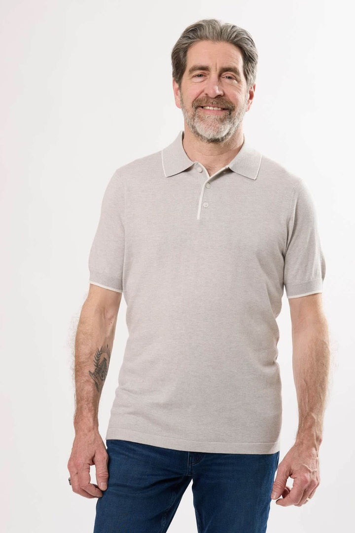Homme souriant portant un polo en tricot fin de couleur beige, avec des manches courtes et col classique.