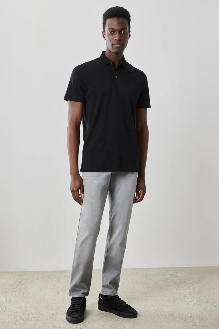 Homme portant un polo manches courtes Georgia noir, associé à un pantalon gris et des baskets noires.