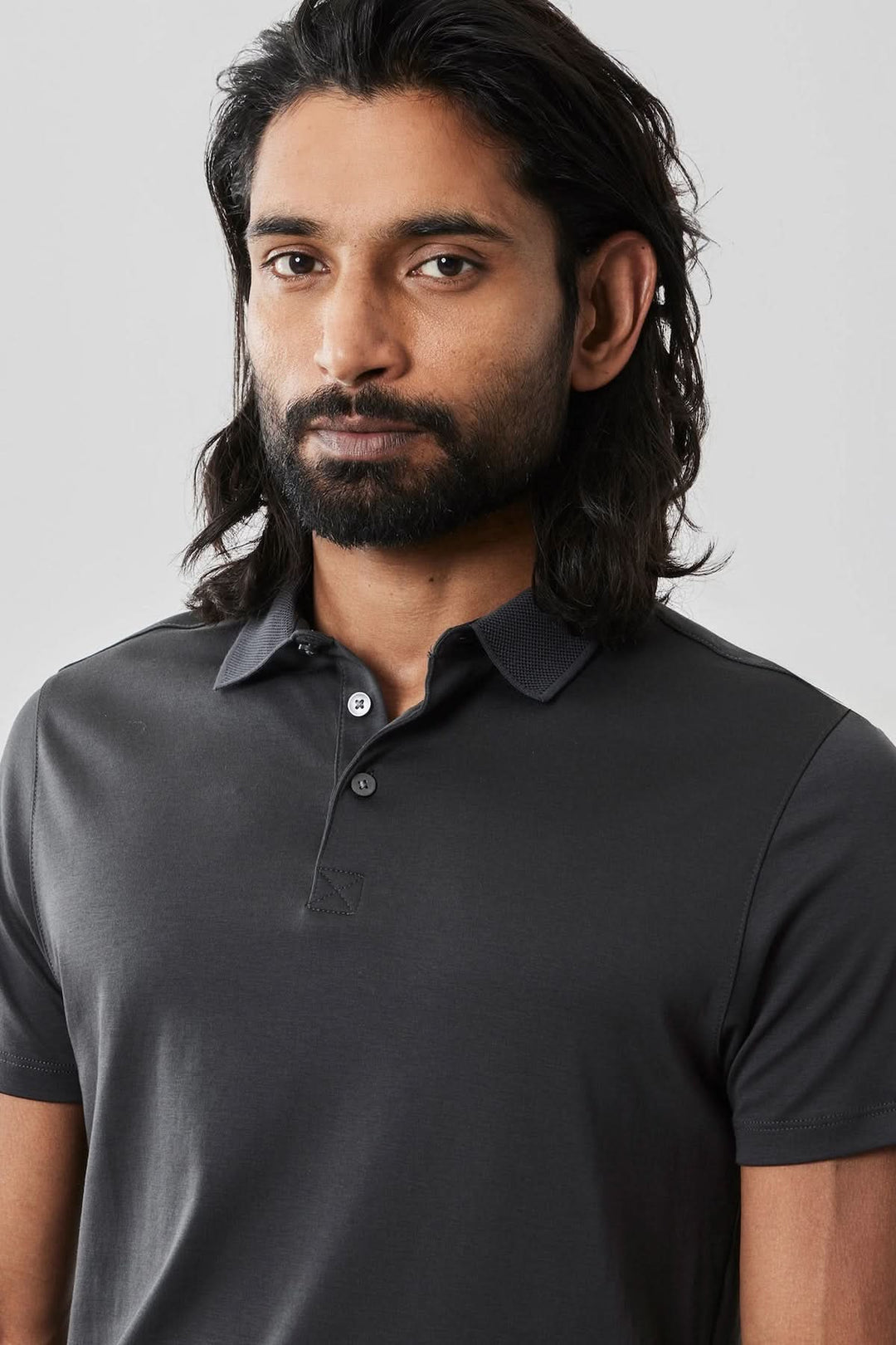 Homme portant un polo noir à manches courtes, col de chemise et patte de boutonnage, style chic et décontracté.