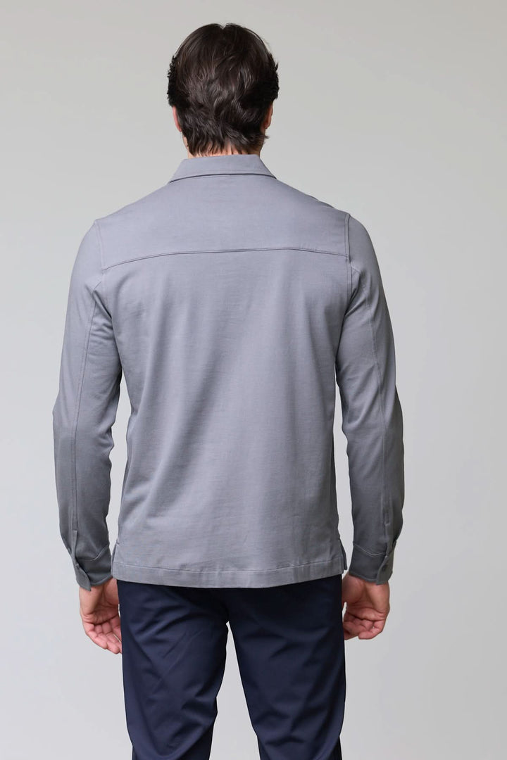 Homme portant un Polo à poches boutonnées gris, vue de dos, avec manches longues et tissu doux, style utilitaire et décontracté chic.