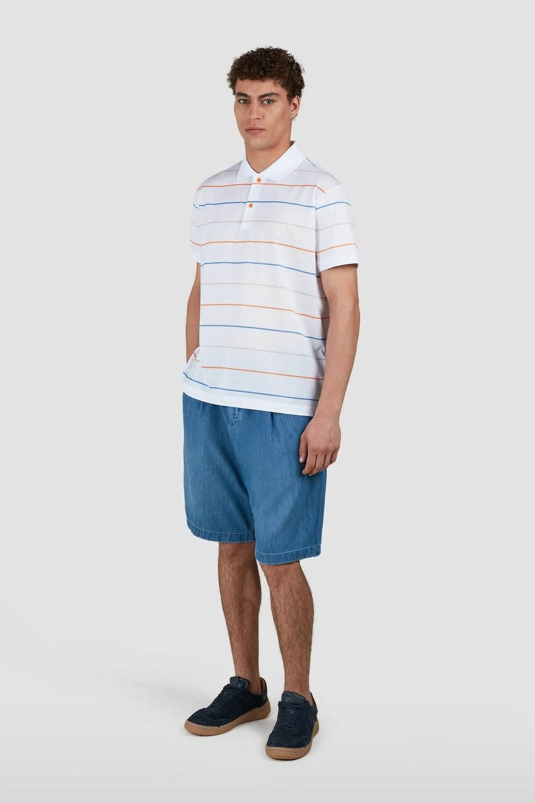Homme portant un polo à rayures multicolores avec un short en denim, idéal pour un look estival décontracté.