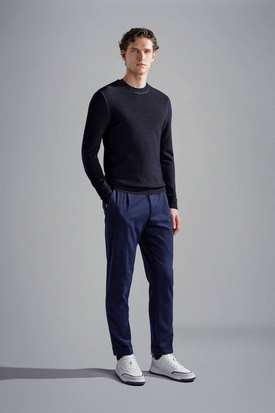 Homme portant un pull en laine mérinos noir avec pantalon bleu et chaussures blanches, offrant un look élégant et moderne.