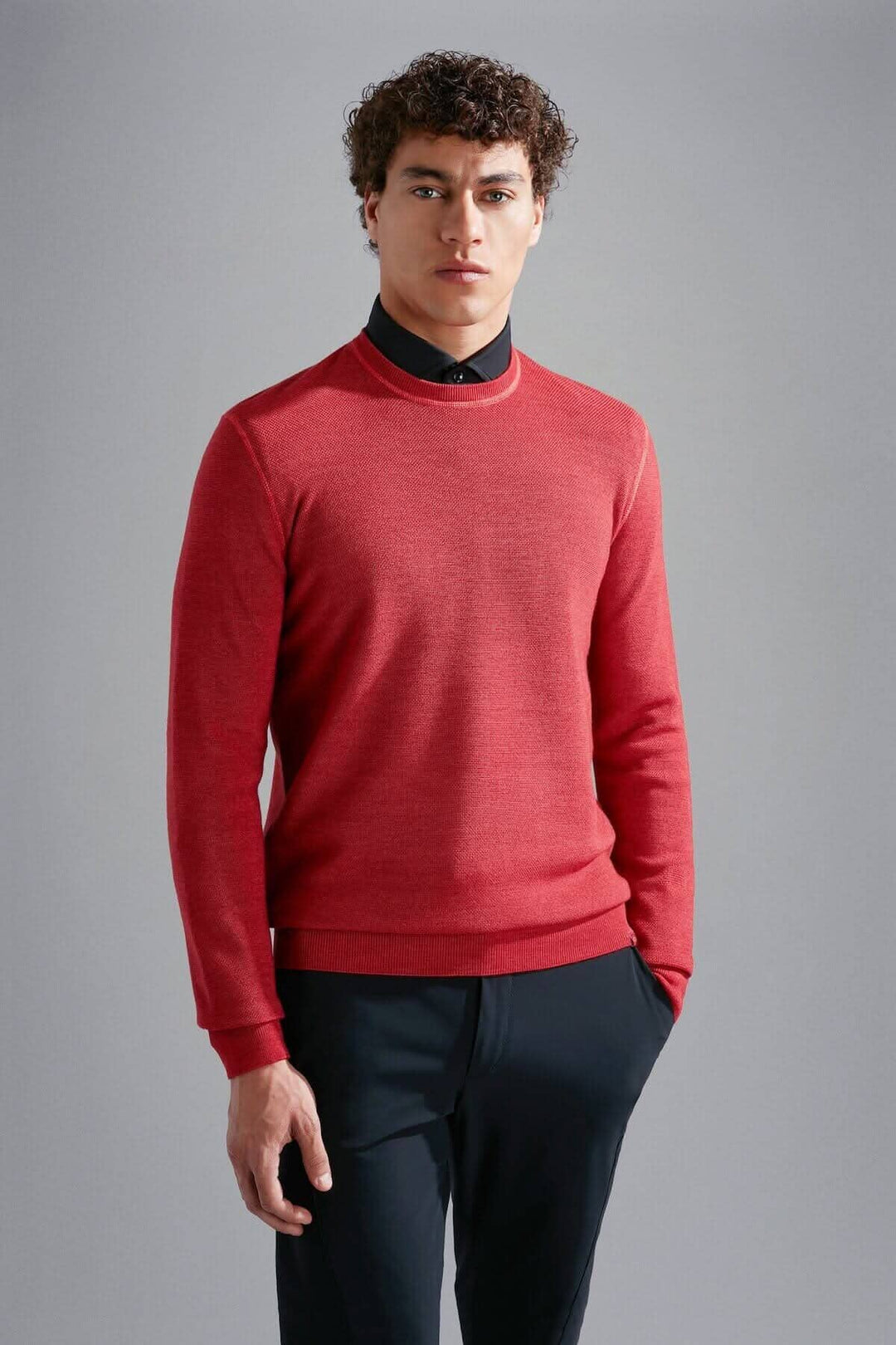 Homme portant un pull en laine mérinos rouge, au col rond, avec une chemise noire pour un look élégant.