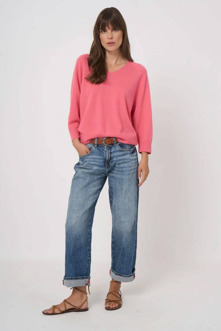 Femme portant un pull en tricot à col en V rose avec jeans décontractés.