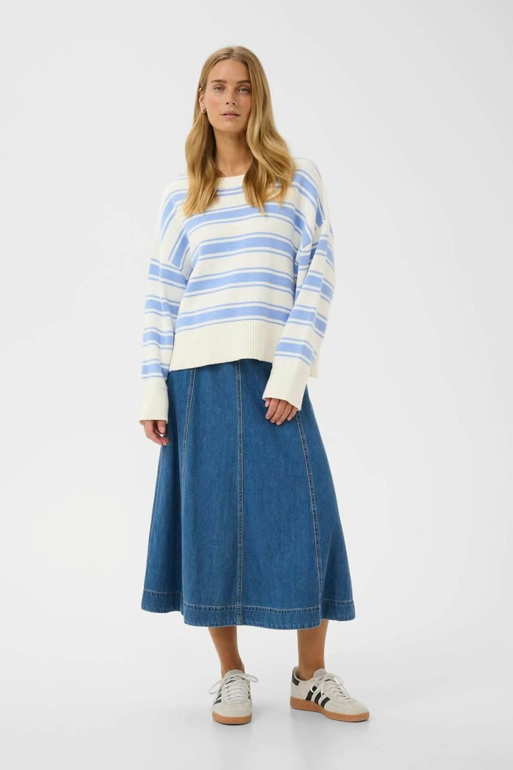 Femme portant un Pull à rayures Serafine avec jupe en denim et baskets blanches, style décontracté et élégant pour temps frais.