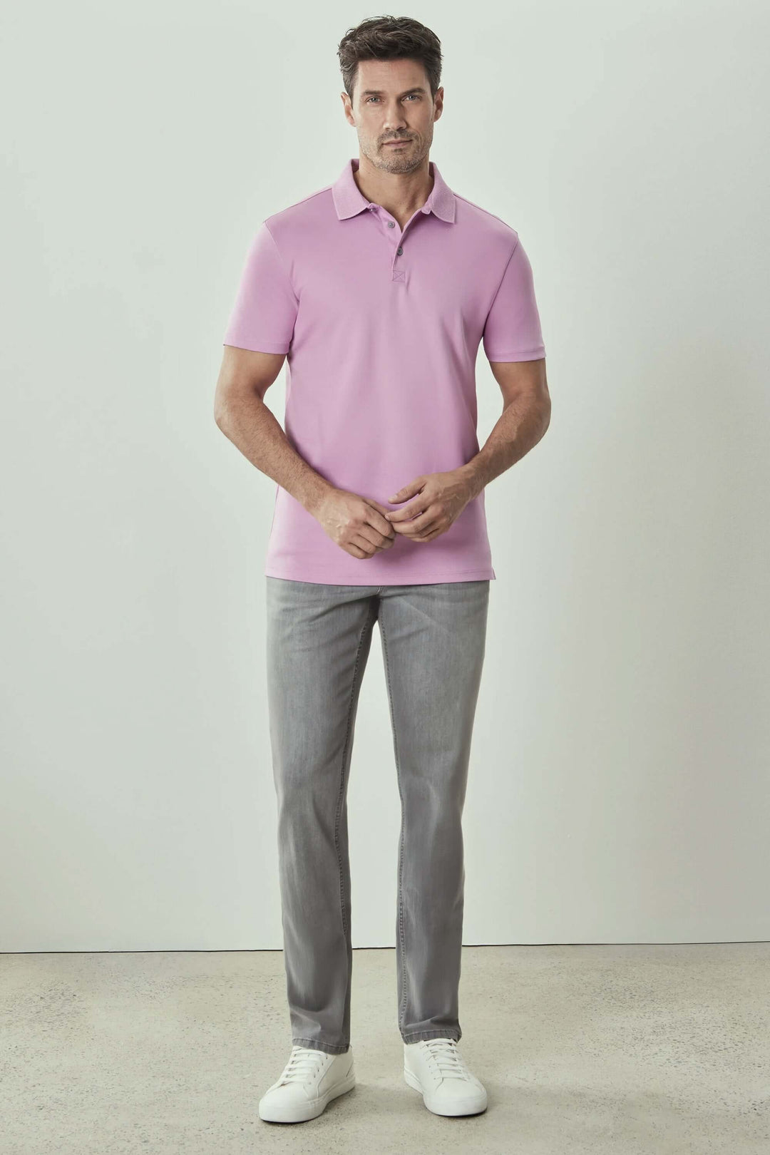 Homme portant un polo manches courtes rose Georgia avec pantalon gris et chaussures blanches.