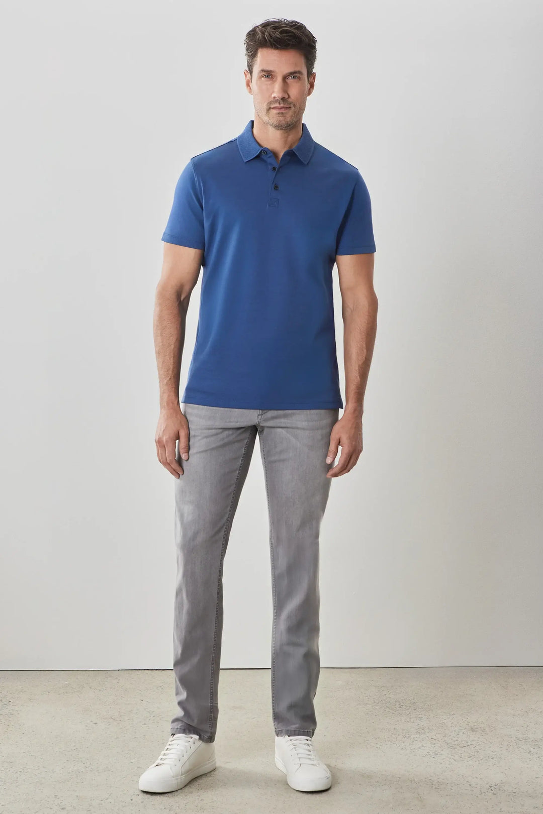 Homme portant un polo manches courtes Georgia bleu avec pantalon gris et baskets blanches, style décontracté.