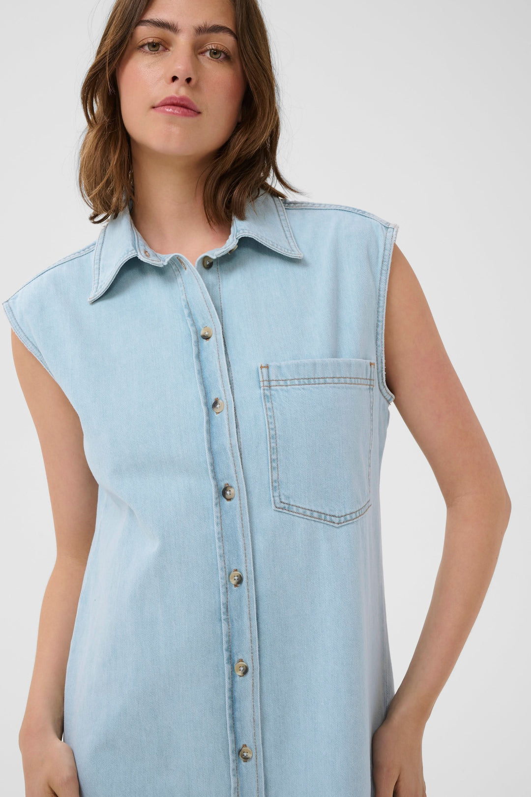 Femme portant Robe Elly chemise sans manches en lyocell avec boutonnière, col structuré et poche poitrine, style décontracté et moderne.