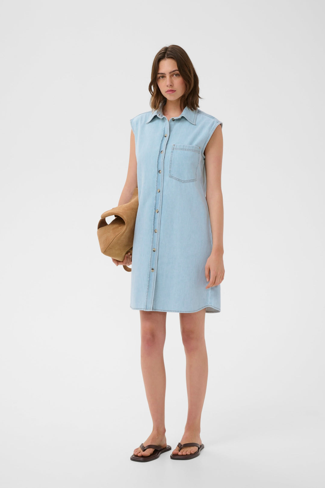 Femme portant la Robe Elly chemise sans manches, coupe droite, col structuré, tissu léger, avec chapeau et sandales pour un look estival.