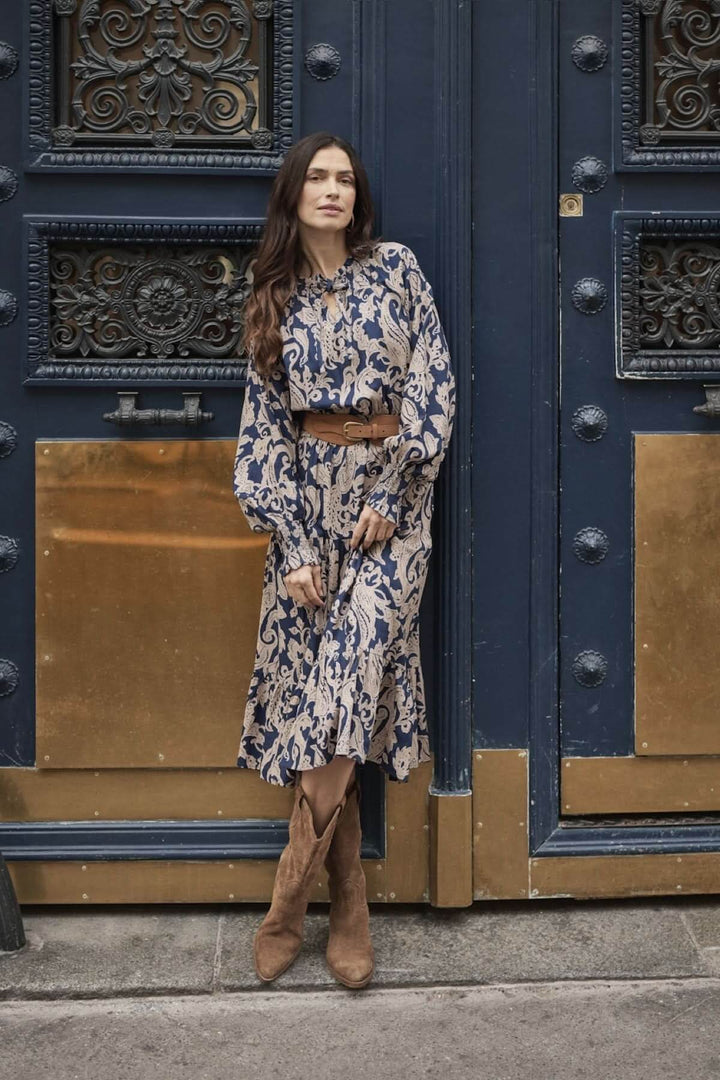 Robe Lucy longue avec motif beige et bleu marine, encolure en goutte, manches longues et ceinture en cuir.