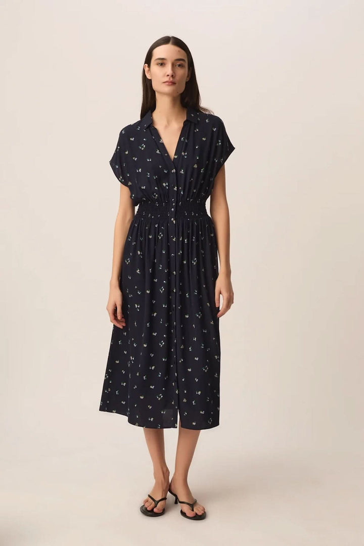 Femme portant la Robe Renaldi midi fluide à taille smockée, manches courtes, encolure en V, tissu léger et motifs délicats.