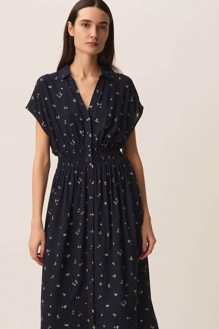 Femme portant la Robe Renaldi midi fluide à taille smockée avec imprimés, encolure en V et manches courtes, silhouette élégante.