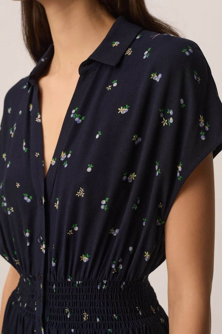 Femme portant la Robe Renaldi midi fluide à taille smockée avec motif floral, encolure en V, manches courtes et tissu léger.