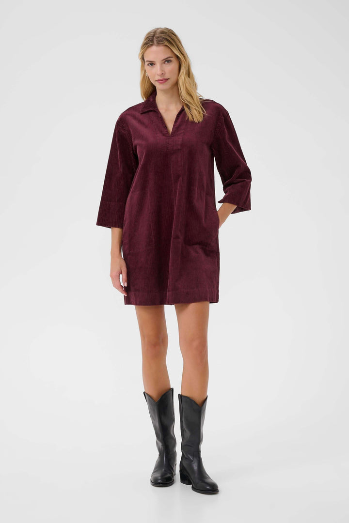 Robe Sharri en velours côtelé bordeaux avec manches trois-quarts et encolure en V, portée avec des bottes noires.