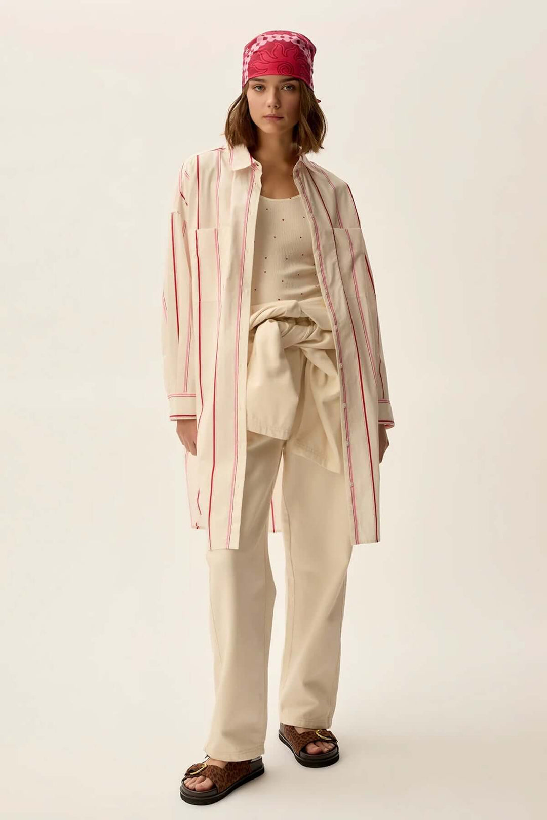 Femme portant une robe longue rayée oversize, coordonnée avec un pantalon beige et un bandana rose.