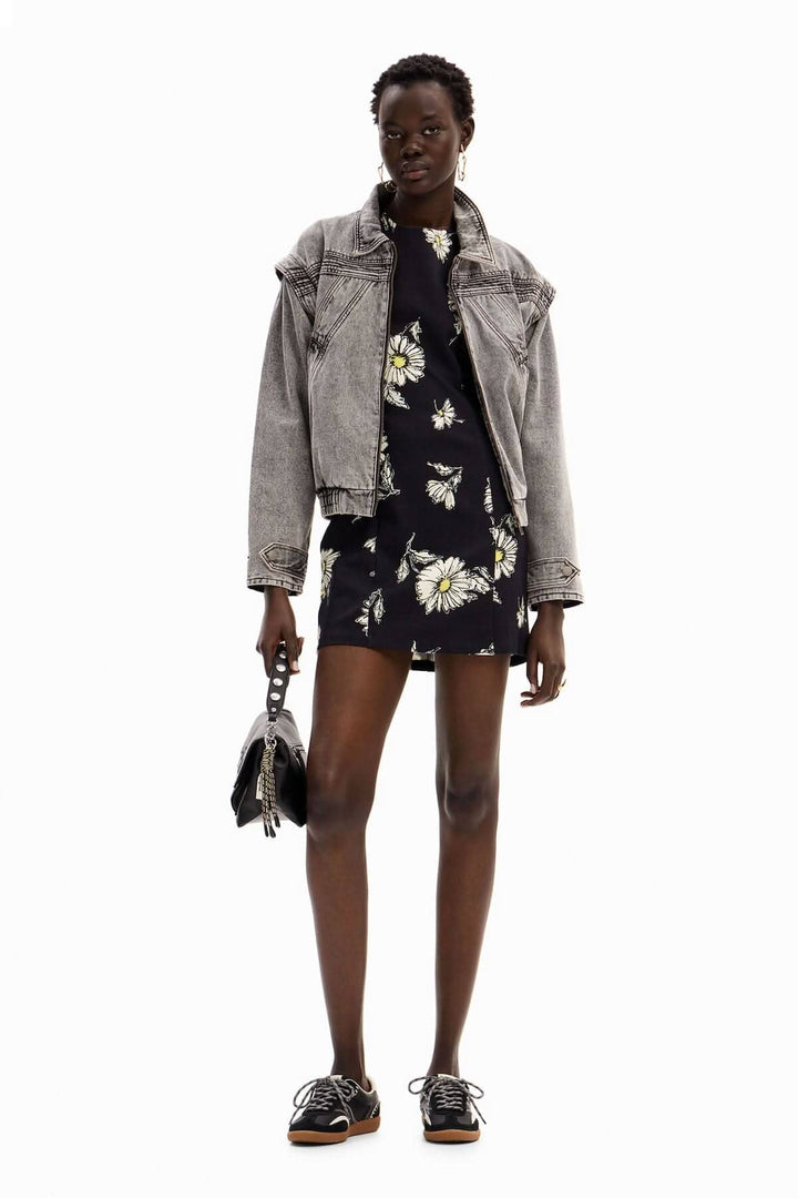 Femme portant une robe courte florale avec une veste en jean grise, idéale pour les journées chaudes.