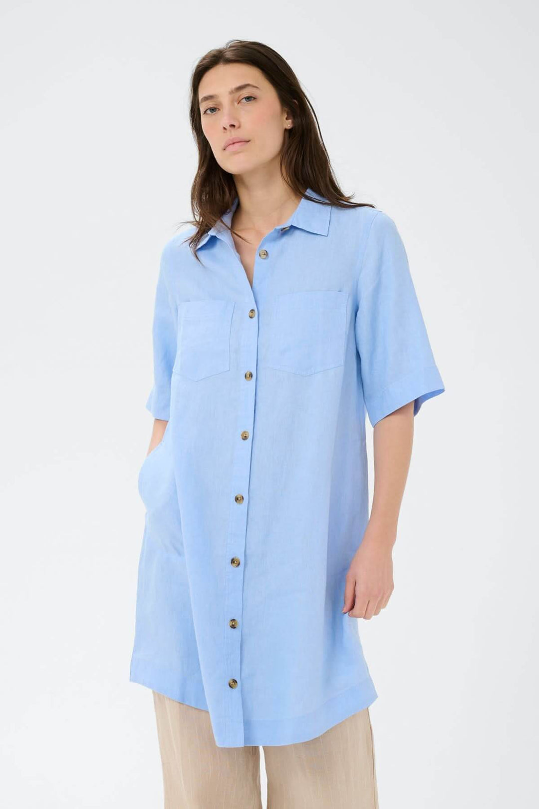 Femme portant une Robe chemise en lin Sardiae bleue avec fermeture boutonnée, coupe droite et manches courtes, style urbain et minimaliste.