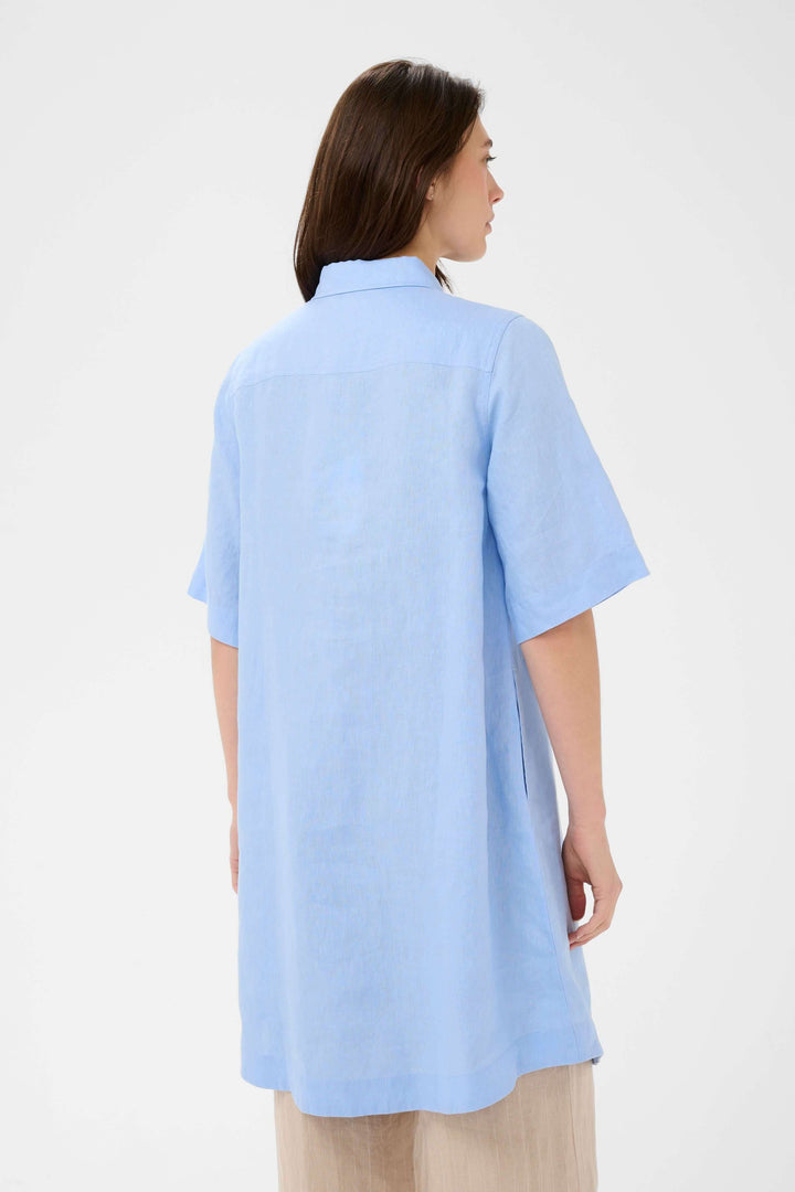 Femme portant une robe chemise en lin Sardiae bleue, vue de dos, avec coupe droite et détails boutonnés pour un look minimaliste.