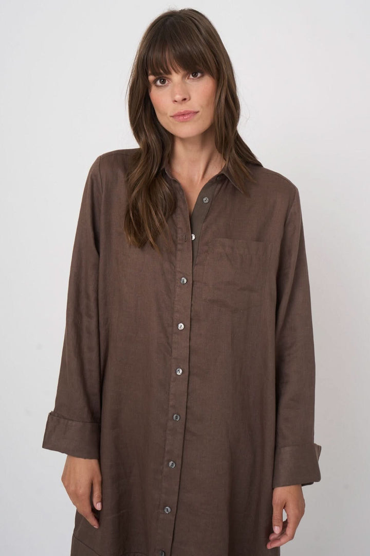 Femme portant une robe chemise à manches longues marron avec fermeture boutonnée et col classique, style décontracté et élégant.