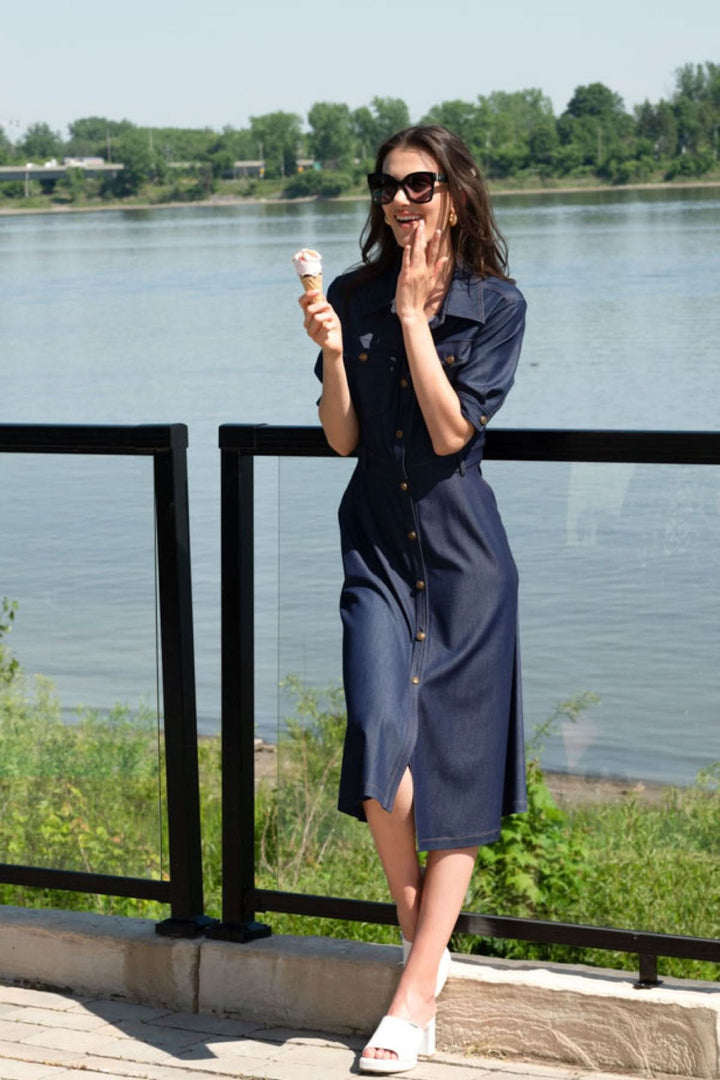 Woman enjoying an ice cream by the river, wearing a stylish denim-look shirt dress on a sunny day.