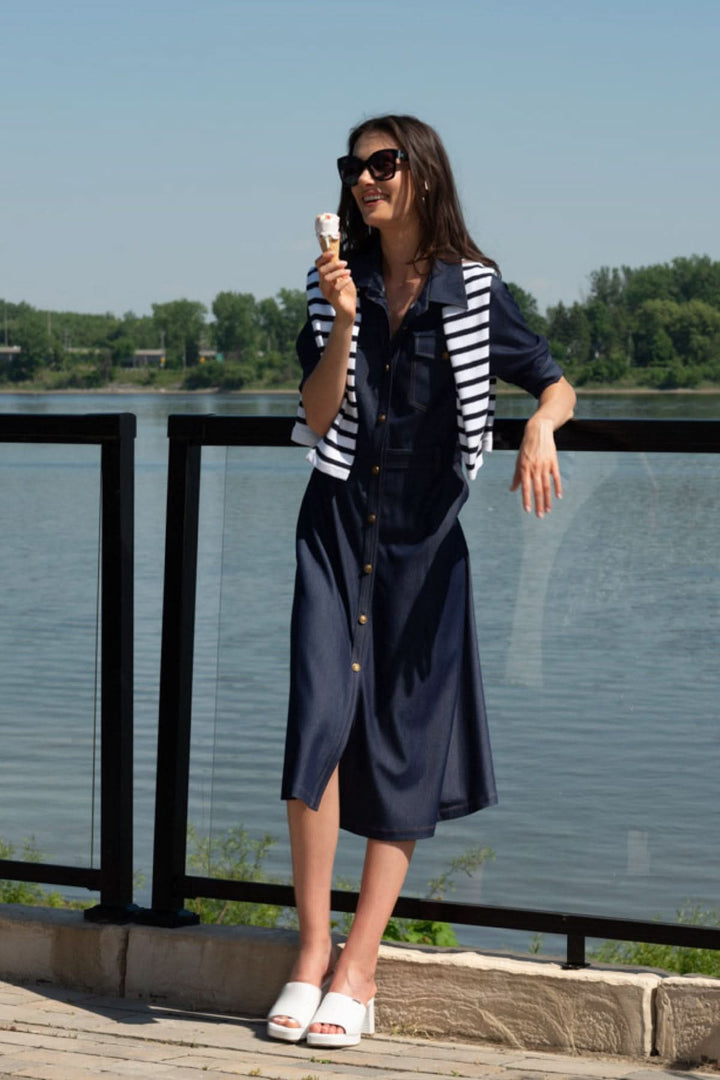 Model wearing a denim-style shirt dress with a striped sweater, enjoying ice cream by the water.