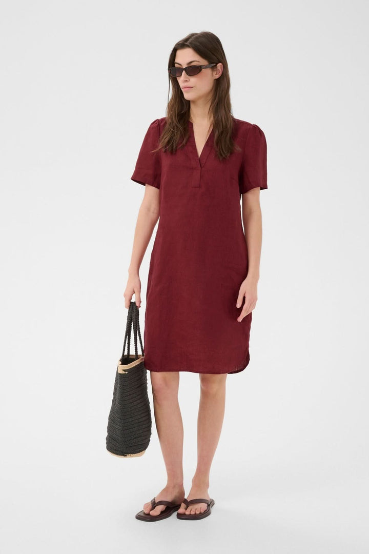 Femme portant une Robe en lin Aminase rouge avec accessoires, debout, mettant en valeur le style élégant et confortable pour toutes occasions.