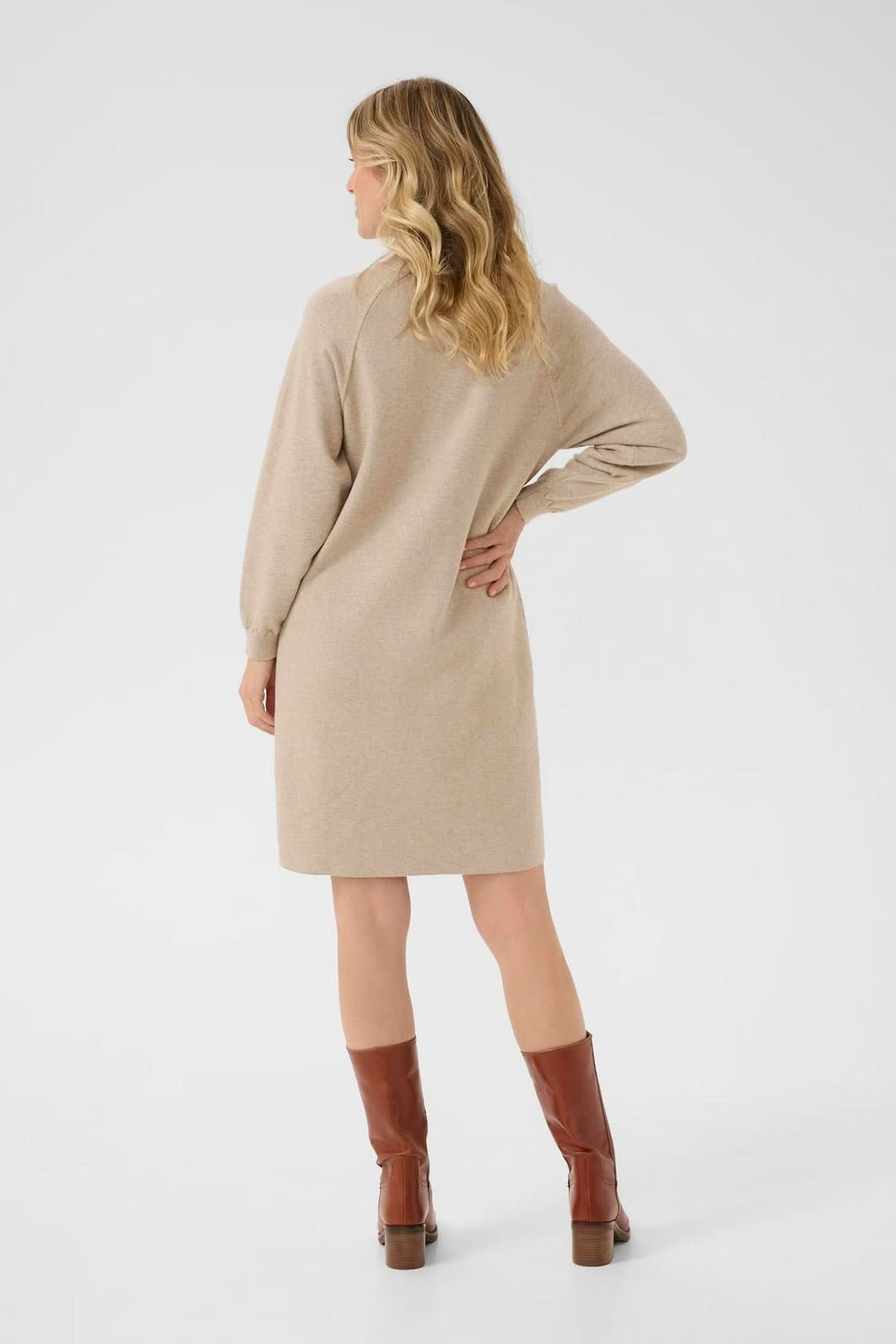 Robe en maille beige à coupe droite, manches longues, portée avec des bottes hautes pour un look décontracté.