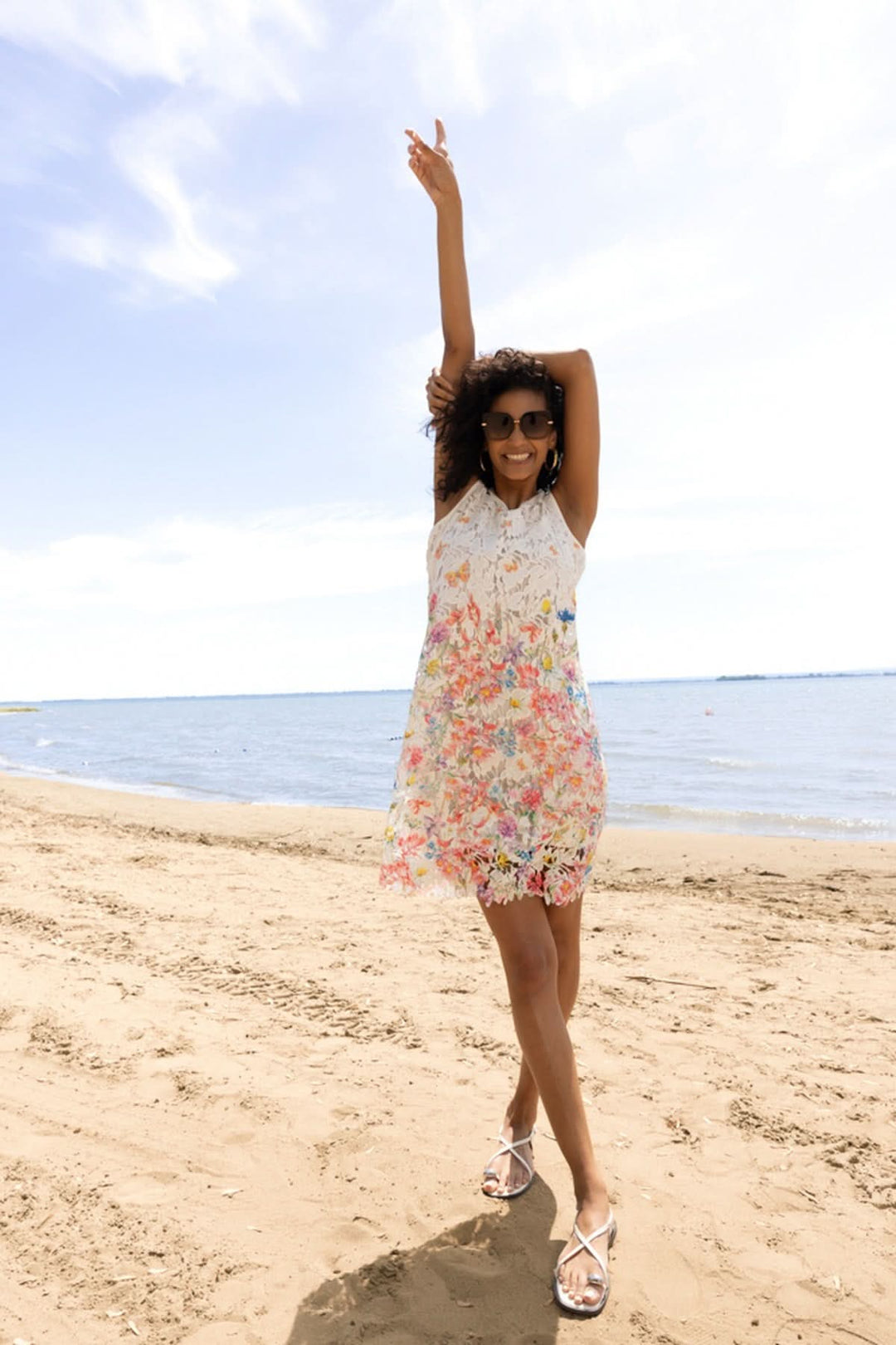 Femme portant une robe florale avec détails sur la plage sous un ciel ensoleillé