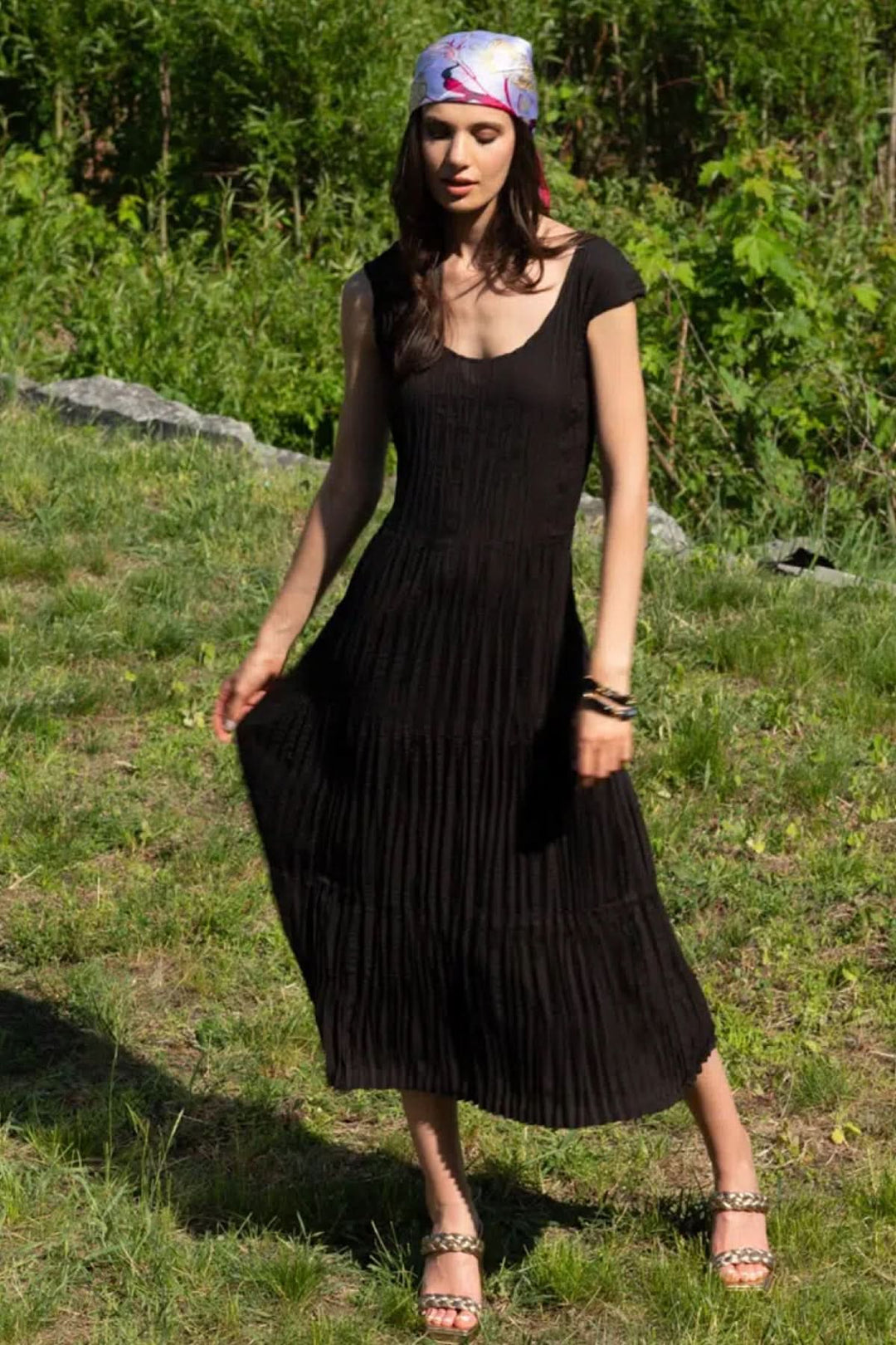 Femme portant une robe longue en tissu plissé noire, élégante et fluide, dans un cadre naturel.