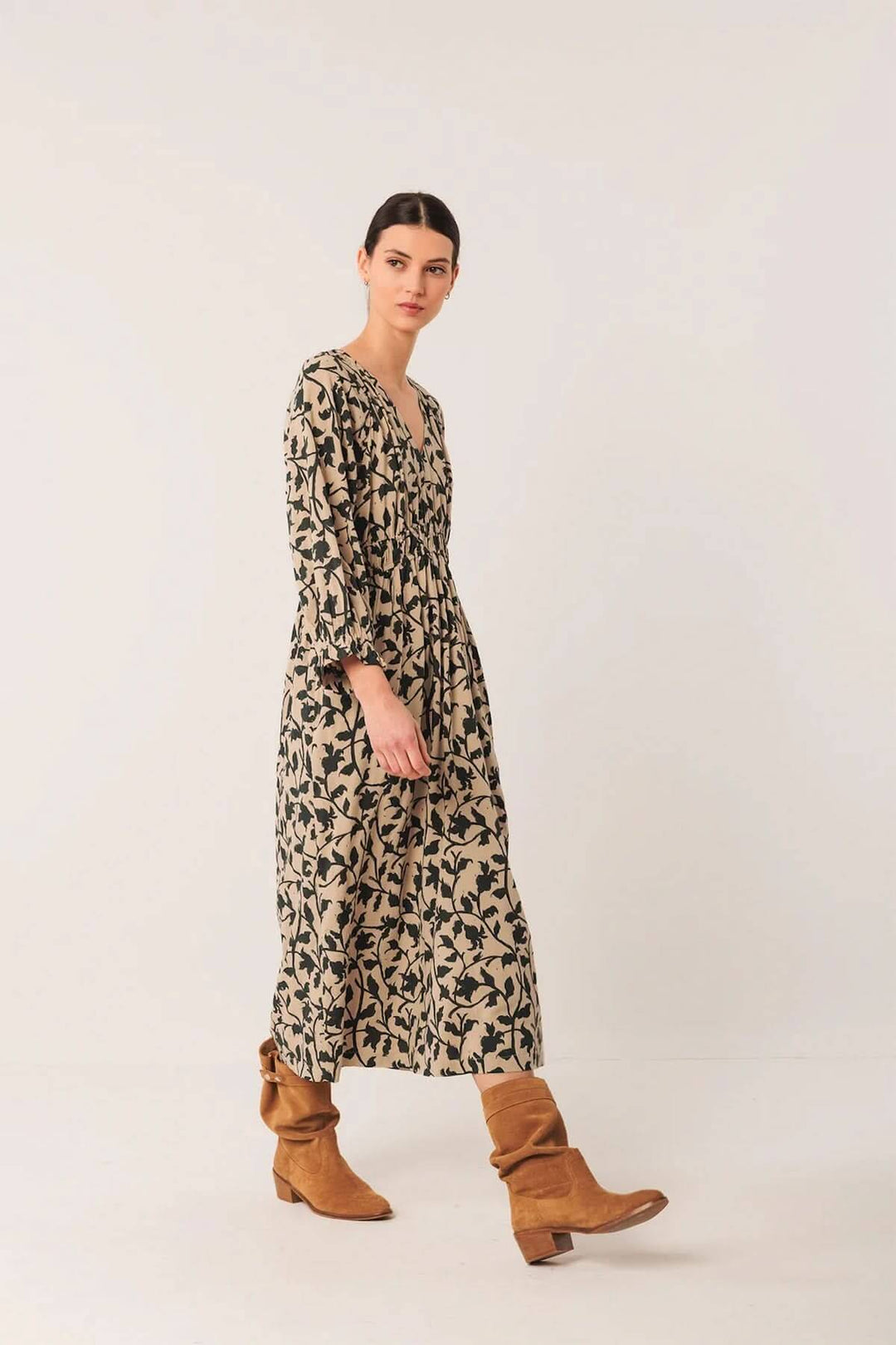 Robe longue fluide imprimé botanique avec décolleté en V, portée avec des bottes en cuir, style bohème.